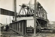 Construction of the Maribyrnong River Bridge on the South Kensington to West Footscray line, Kensington, 1928. A 32 ton girder for the approach span has been lifted into place while chains from a crane are being attached to a second girder.