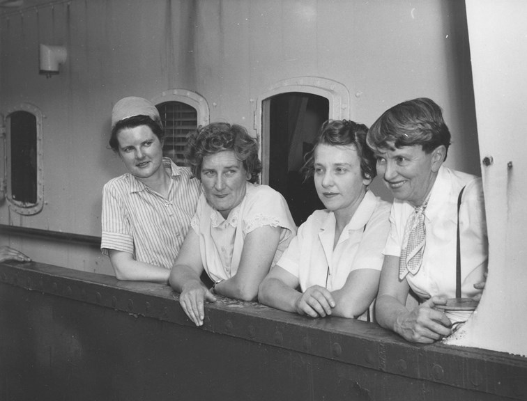 Four women look over the balcony of a ship. 
