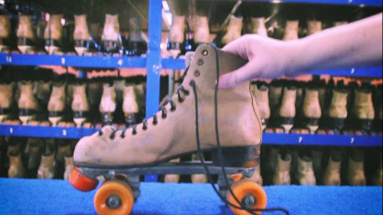 Still of a hand holding a roller skate in front of shelves of multiple roller skates