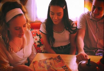 Still of three people sitting around a table looking at a magazine