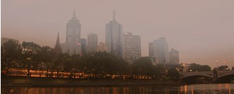 Wide shot of Melbourne city from the Southbank side, across the river, covered in smog, with a bridge in the background