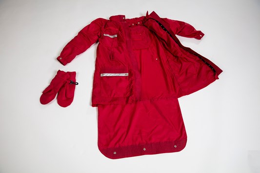 A red jacket is laid out flat on the ground and is opened up to display various components, such as gloves and storage compartments.