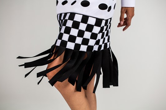 A detail of the bottom of the dress. It has black and white strips woven to create a checkered effect and black fringing that is responsive to movement. 