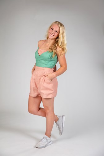 A model is seen from the front wearing a pink linen playsuit. A green reversible crop top is worn over the top. 