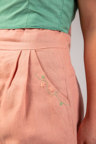 A detail of a pink linen playsuit. There is pink and green floral embroidery on the pcoket