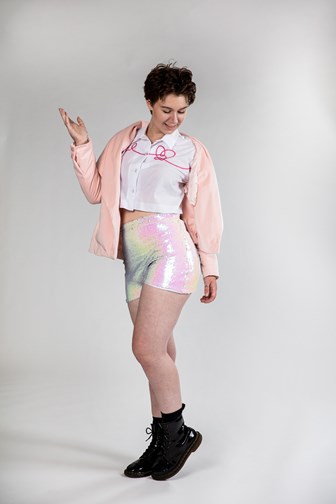 A girl is dancing wearing sequined shorts, a cotton shirt with pink embroidery and a pink velvet jacket.
