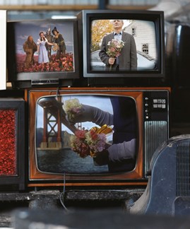 Close up of three televisions stacked on top of each other with images of people with flowers