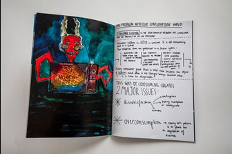 A photograph of an open art zine showing two pages, one colourful page with colourful illustration of the devil holding a television, the other is a white page with black text, in a hand-written style