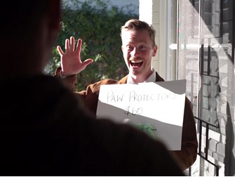 A resident greets a young man with a manic smile holding a sign advertising paw protectors for sixty dollars at their door