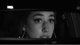 A close up of a girl wearing hoop earrings in the rear view mirror of a car.  She is looking at something in the mirror and looks frightened.