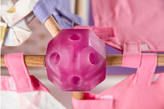 A close up of a multi-faceted pink resin ball that wooden poles are inserted into. Pink, purple and white fabric tabs are seen either side. 