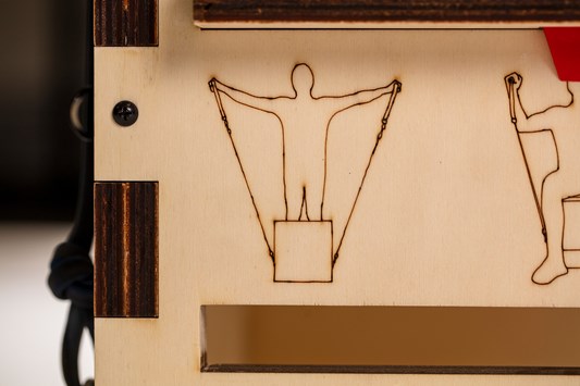 A detail of an illustration, on a wooden panel, of a person doing a stretching exercise. It is a simple outline of a figure that has been laser cut into the wood.