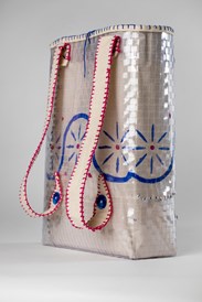 A bag created by weaving a lattice of plastic. It has two straps made of out calico, to be worn as a backpack. It has a pink and blue blockprint pattern of a flower accross the front.