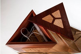 A top view of a wooden table made from light and dark brown woods.  It has a glass top. A triangular lid lifts off the top to reveal a charging station. 