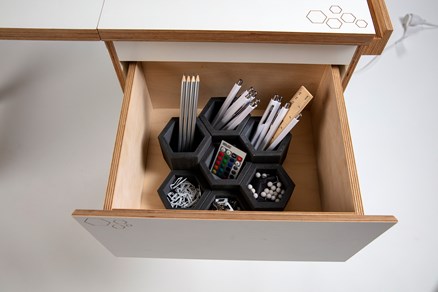 A detail of the top drawer open to display a set of hexagonal desk organisers, filled with stationary. 