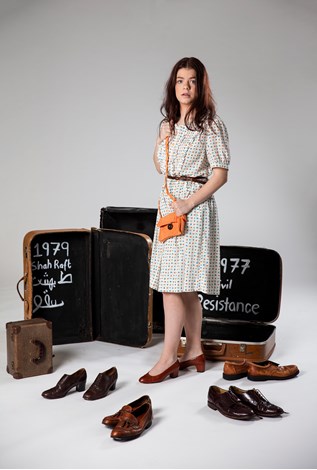 Girl in dress standing amongst open suit cases and pairs of shoes 