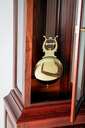 Glass ront case of a wooden grandfather clock open to reveal the metal pendulum 