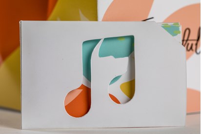 Close-up of a card with a musical quaver cut from the middle, revealing blue, yellow and orange colours behind