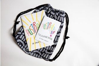 Two colourful books titled 'Australia Alive' sit closed on top of a black and white patterned backpack
