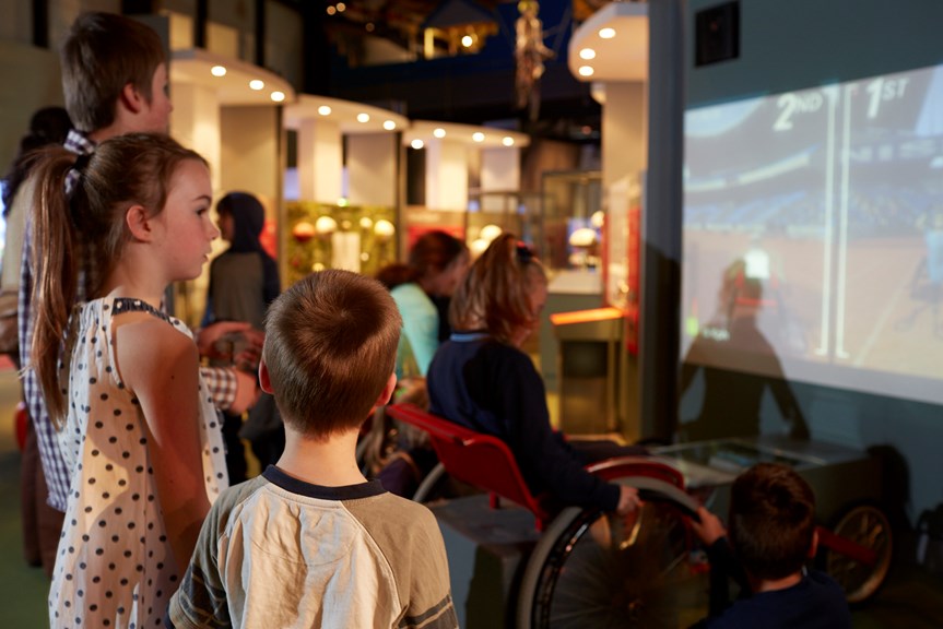 Family surrounding wheelchair interactive in Sportsworks exhibition
