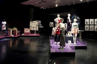 Exhibition display featuring mannequins, furniture and prints