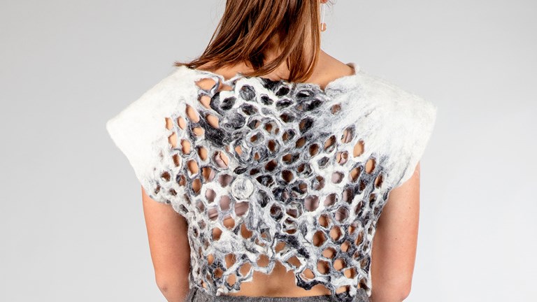 A white felted top, seen from the back. The back has a grey marbelled tessellated detail. The top is held together with felted pegs. 