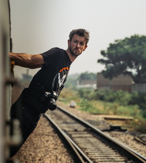 Man leaning out of a train with a camera around his neck