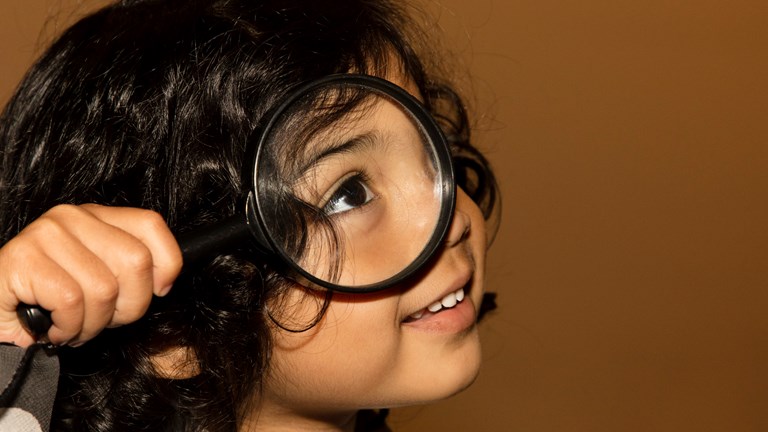 Child holding a magnifying glass up to their face