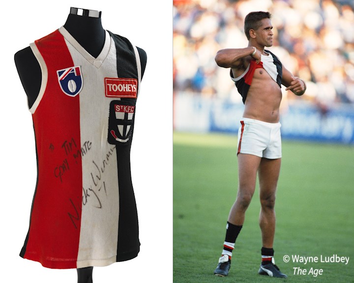 A St Kilda guernsey and a photograph of an Aboriginal footballer raising his top and pointing proudly at his skin. 