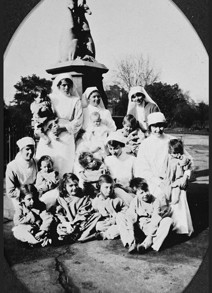 Black and white photo of nurse and children near a fountain