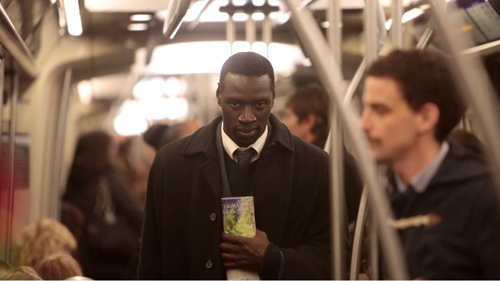 A young man stands on a train clutching a brochure