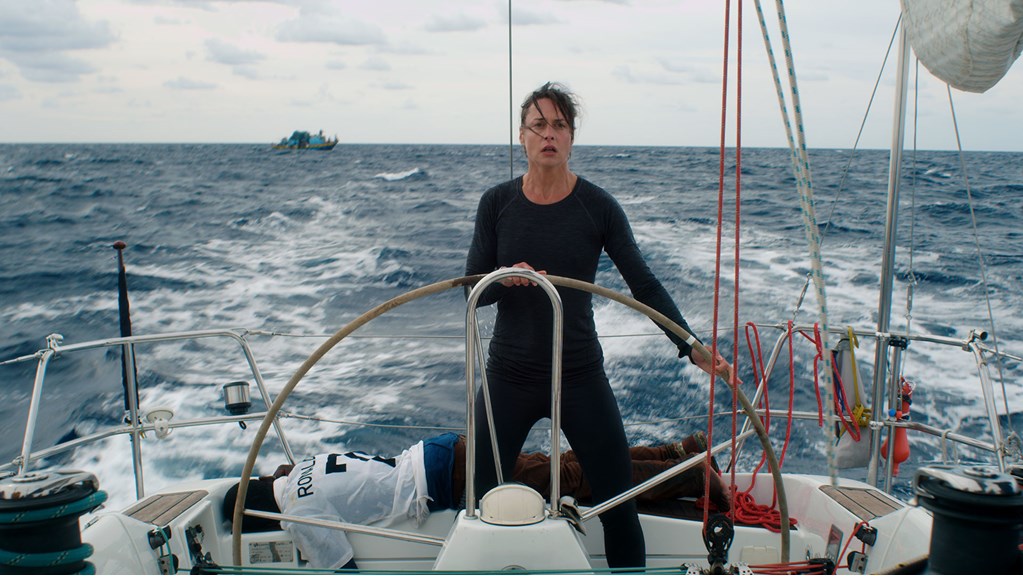 A woman standing at the helm of a yacht, with a concerned/concentrated expression