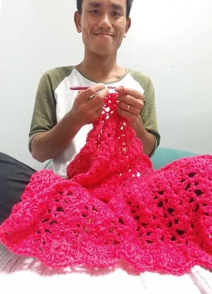 Person sitting cross legged crocheting a red blanket
