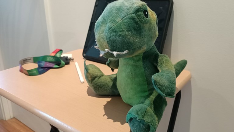 Stuff toy dinosaur sitting on a small card table