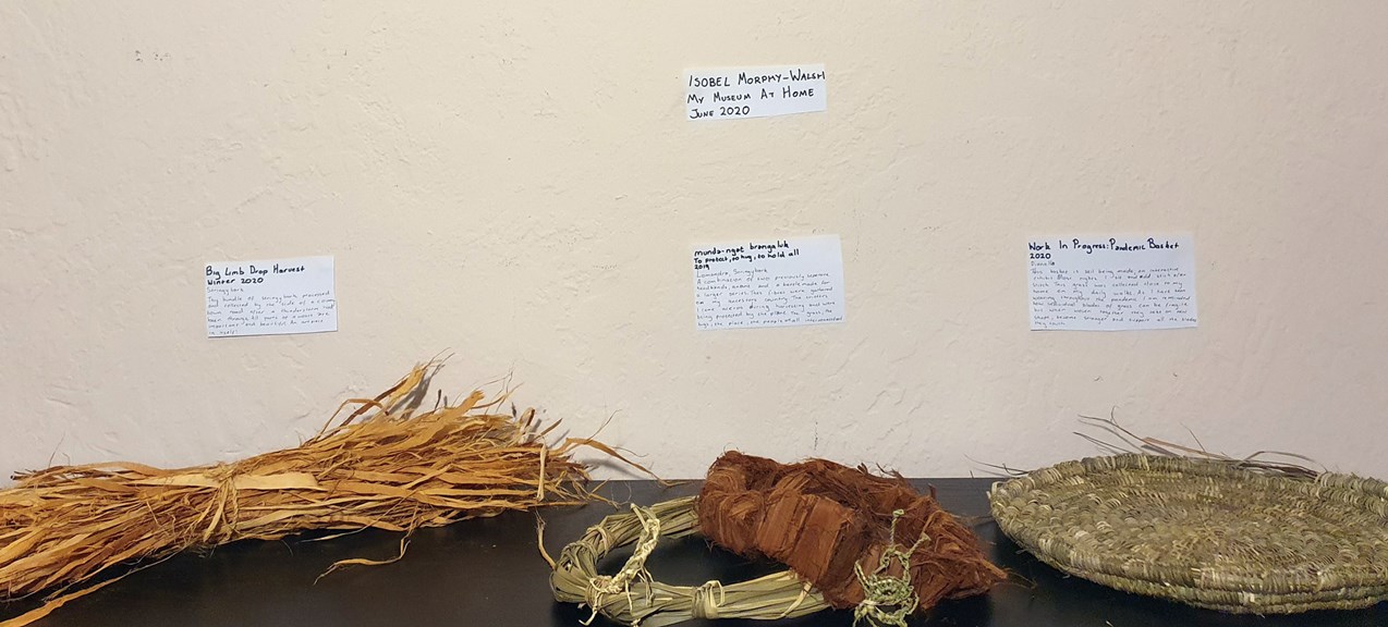 A display of grasses and weaving on a bench top. There are handwritten labels on the wall.