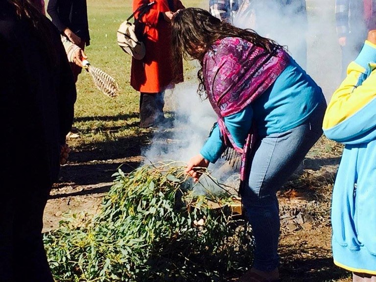 A woman leans into a pile of smoking gumleaves.