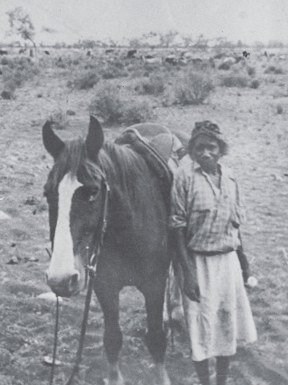 A black and white photograph of a woman standing beside a horse.