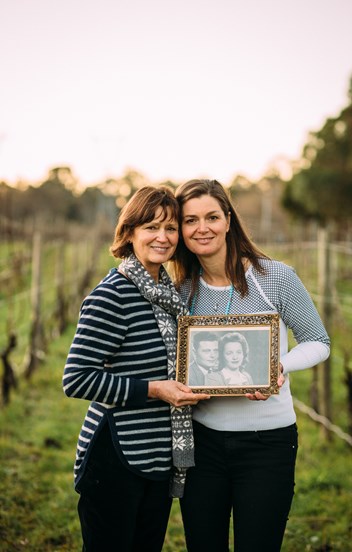 Two women in a vineyard holding a black and white photo. 