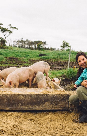A farmer nurses her toddler amid a paddock of chickens and pigs. 