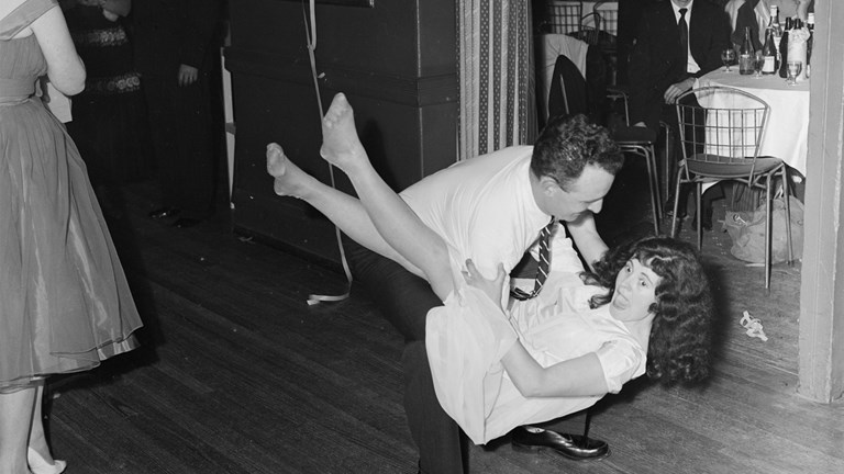 Couple dancing at a Swallow & Ariell social function held at 9 Darling Street reception center. The man is lifting the woman off the ground, behind them are people seated at tables.