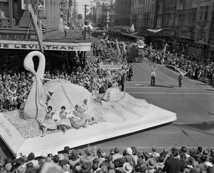 Miss Moomba Float. The 1958 Moomba Parade turning from Bourke St. into Swanston St. A 'City of Melbourne' float with large swan and a group of 'Miss Moomba ' girls passing.