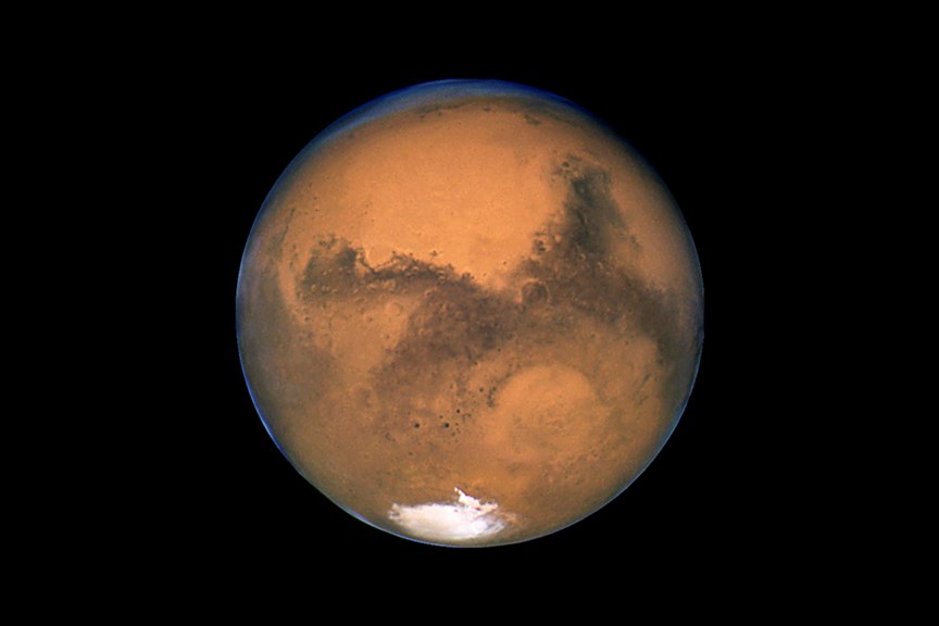 Mars in August 2003 at 56 million km, its closest to Earth in 60,000 years. Clearly visible is the white South Polar Cap, the large circular depression Hellas Basin lower right, the vast upland region Arabia Terra top centre, and two major craters; Schiaparelli (459km) centre left and Huygens (467km) centre right in the dark lowland area. 