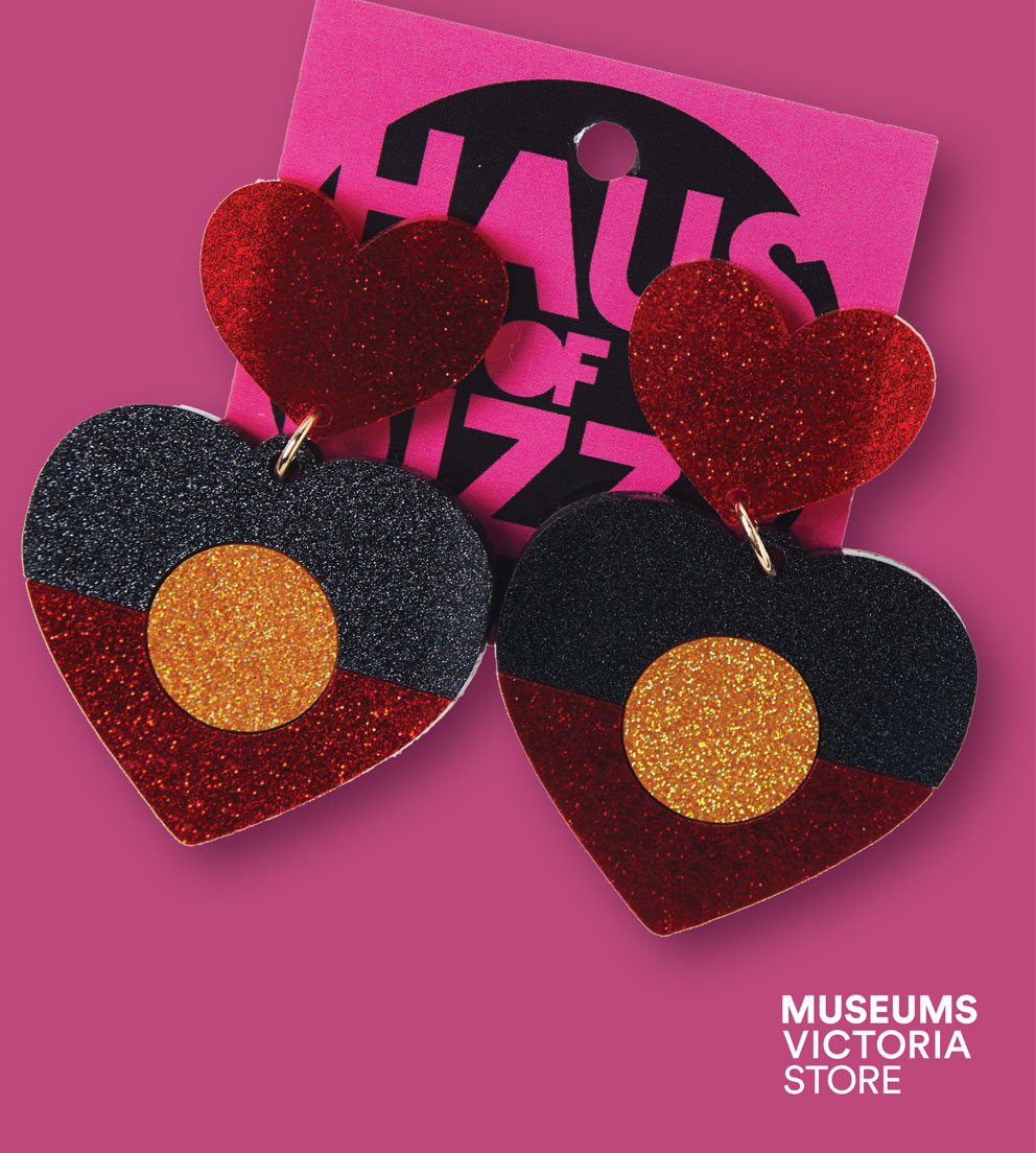 Flay lay image of a pair of heart shape earrings depict the Aboriginal flag on a pink background