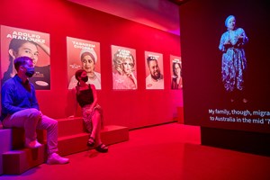 Man and woman viewing a screen in an exhibition. The gallery is lite in red.