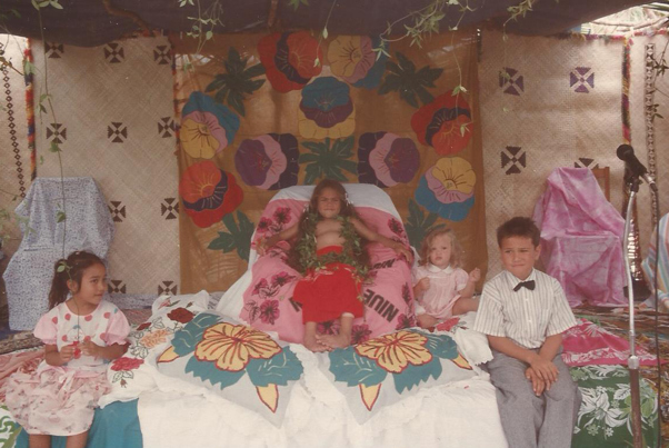 Four children sitting on platform. One is sitting on a ceremonial chair