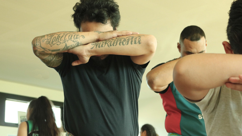 Man standing with his head down and arms crossed in front of him displaying his tattoos