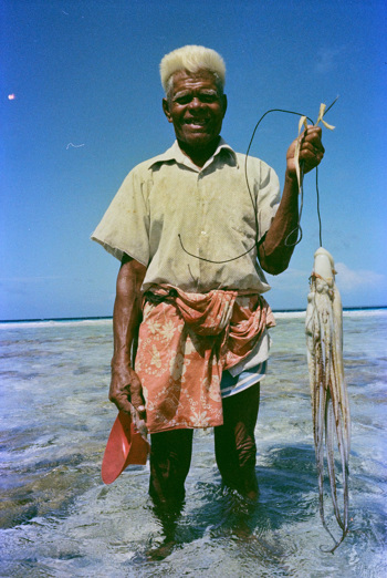 Man standing in ankle deep water holding a squid
