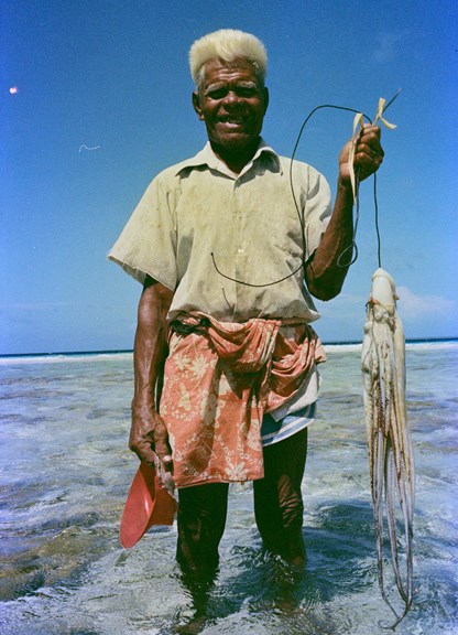 Man standing in ankle deep water holding a squid