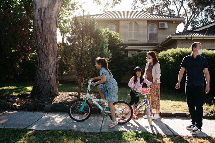 Family of four outside their suburban home. The two girls are riding bikes