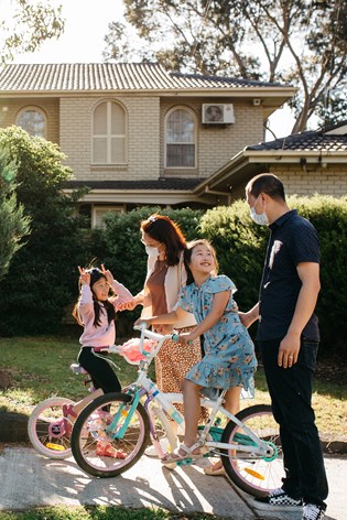 Family of four outside their suburban home. The two girls are riding bikes